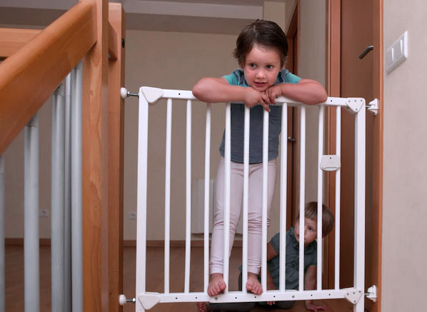 petitite fille et son petit frére derrière une barrière d'escalier à pression